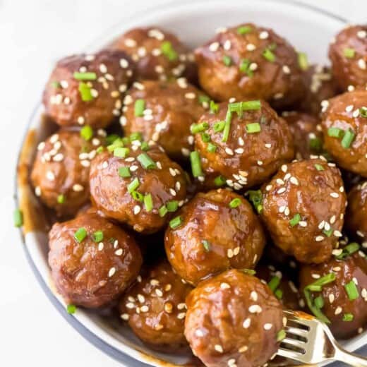 Crockpot Asian meatballs piled into a small bowl with a fork stabbing into one of them