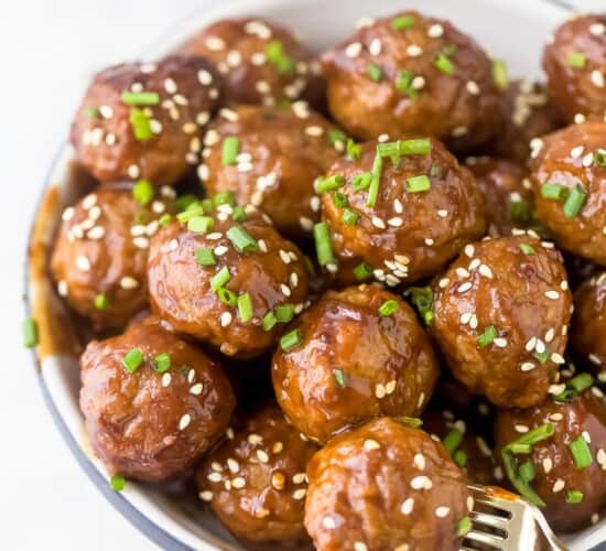 Crockpot Asian meatballs piled into a small bowl with a fork stabbing into one of them