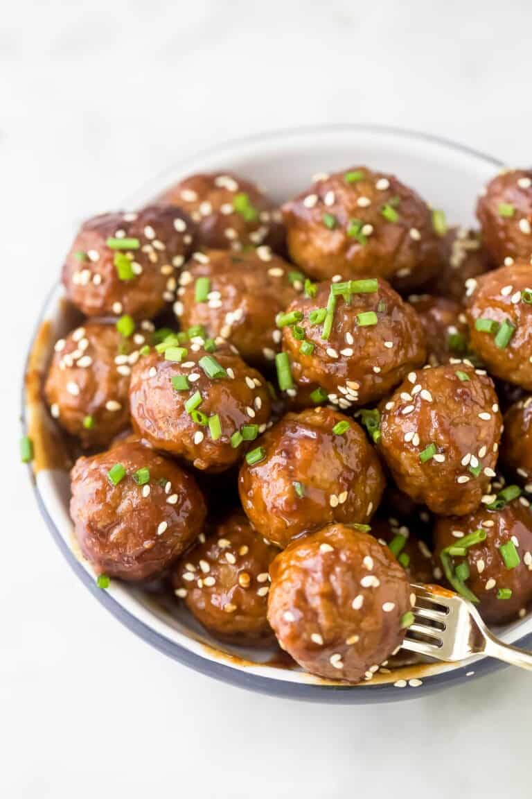 Crockpot Asian meatballs piled into a small bowl with a fork stabbing into one of them