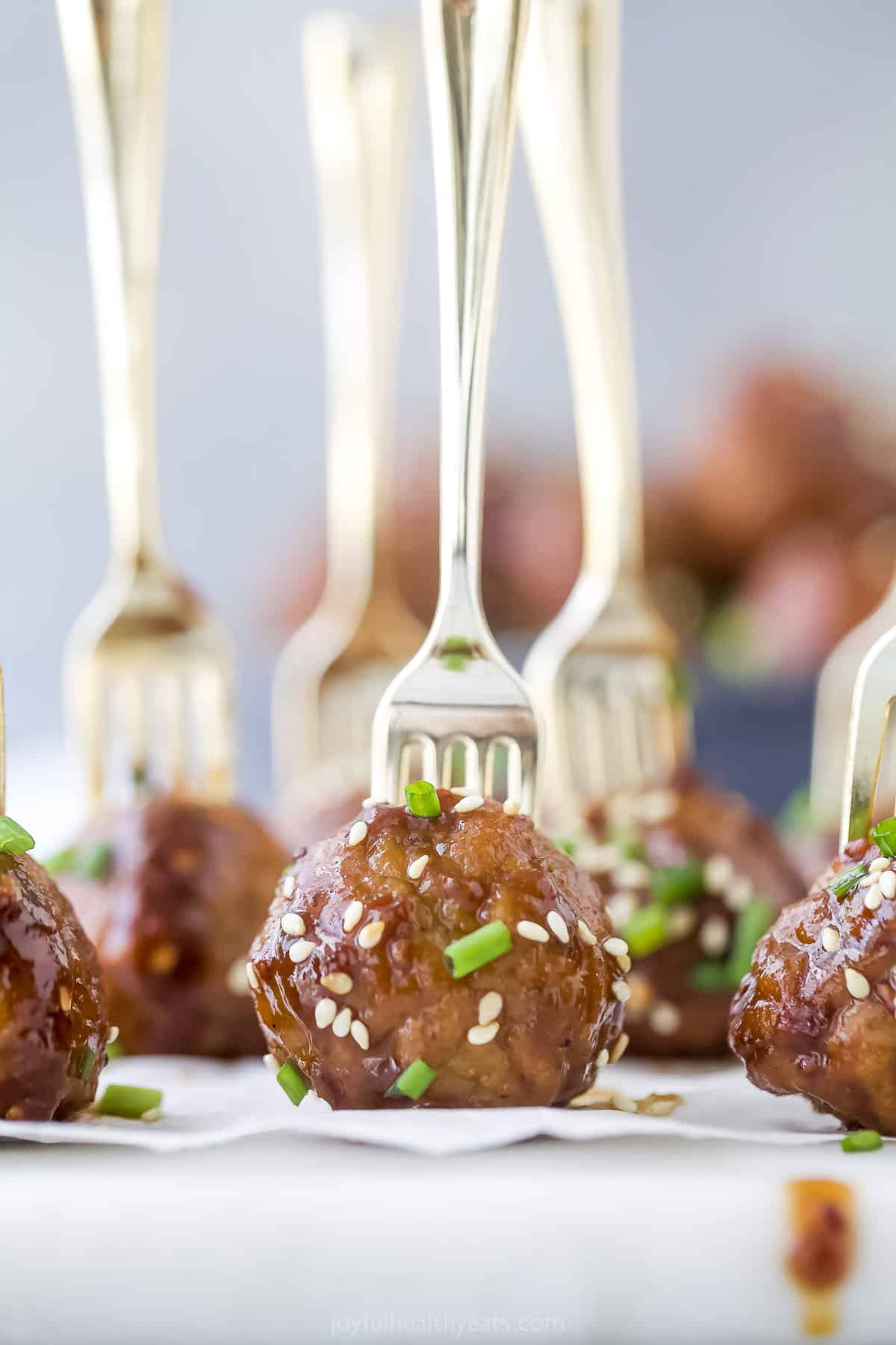 Asian meatballs on a sheet of parchment paper with a fork stuck into each one