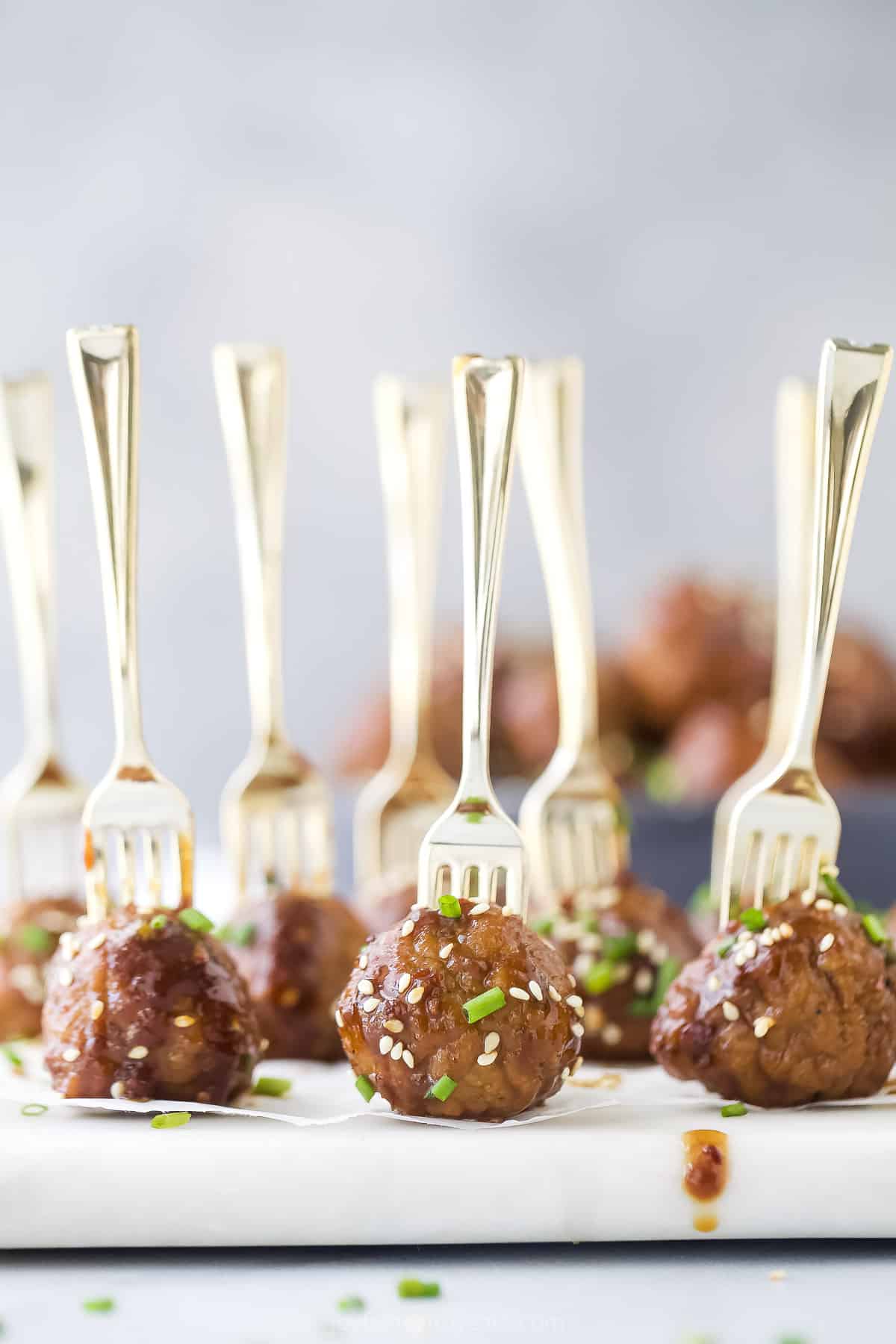 A white cutting board holding Crockpot Asian meatballs with forks jabbed into them