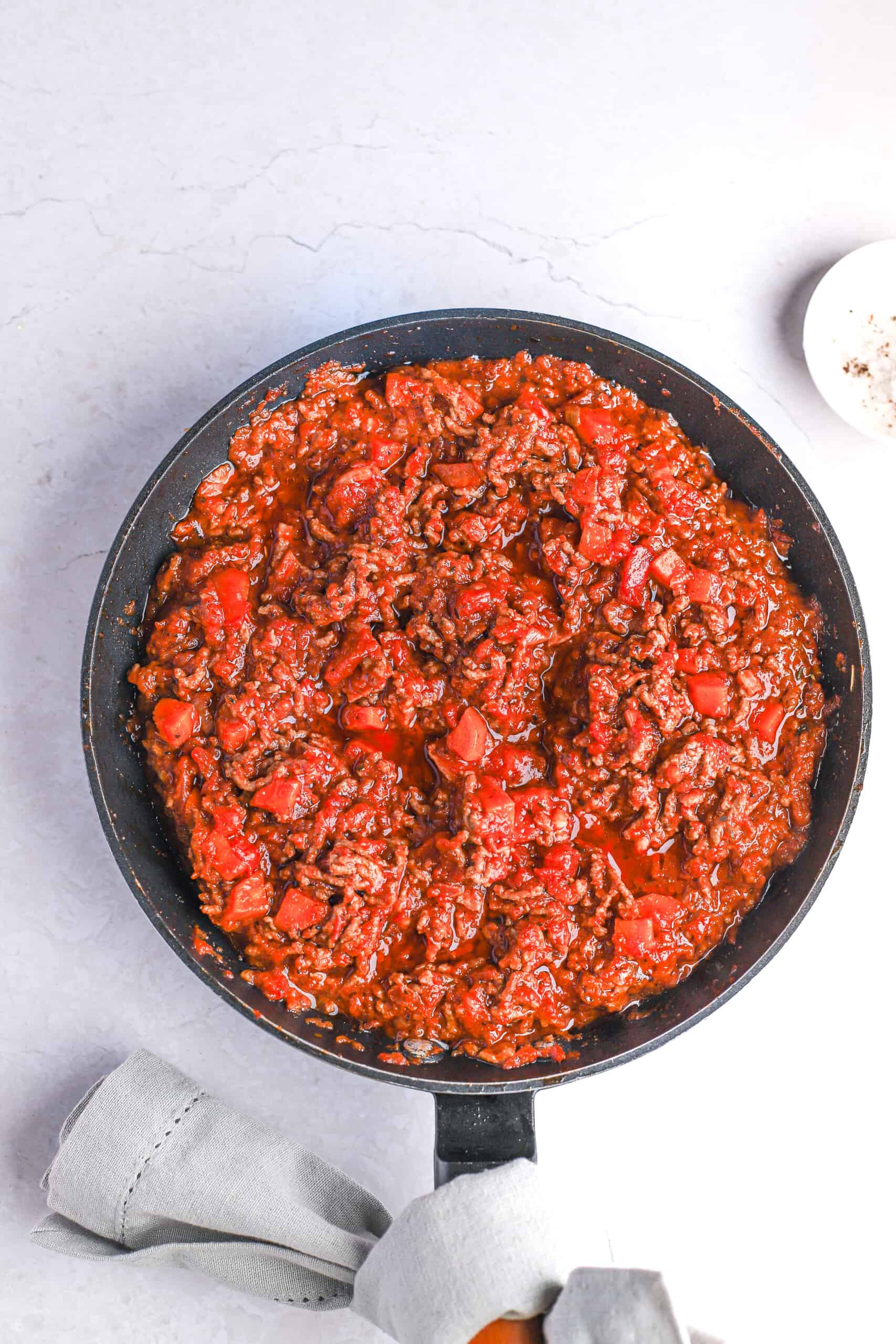 A skillet full of homemade bolognese sauce with a towel tied around the handle