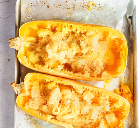 Two halves of a baked spaghetti squash on a parchment-lined pan with a fork