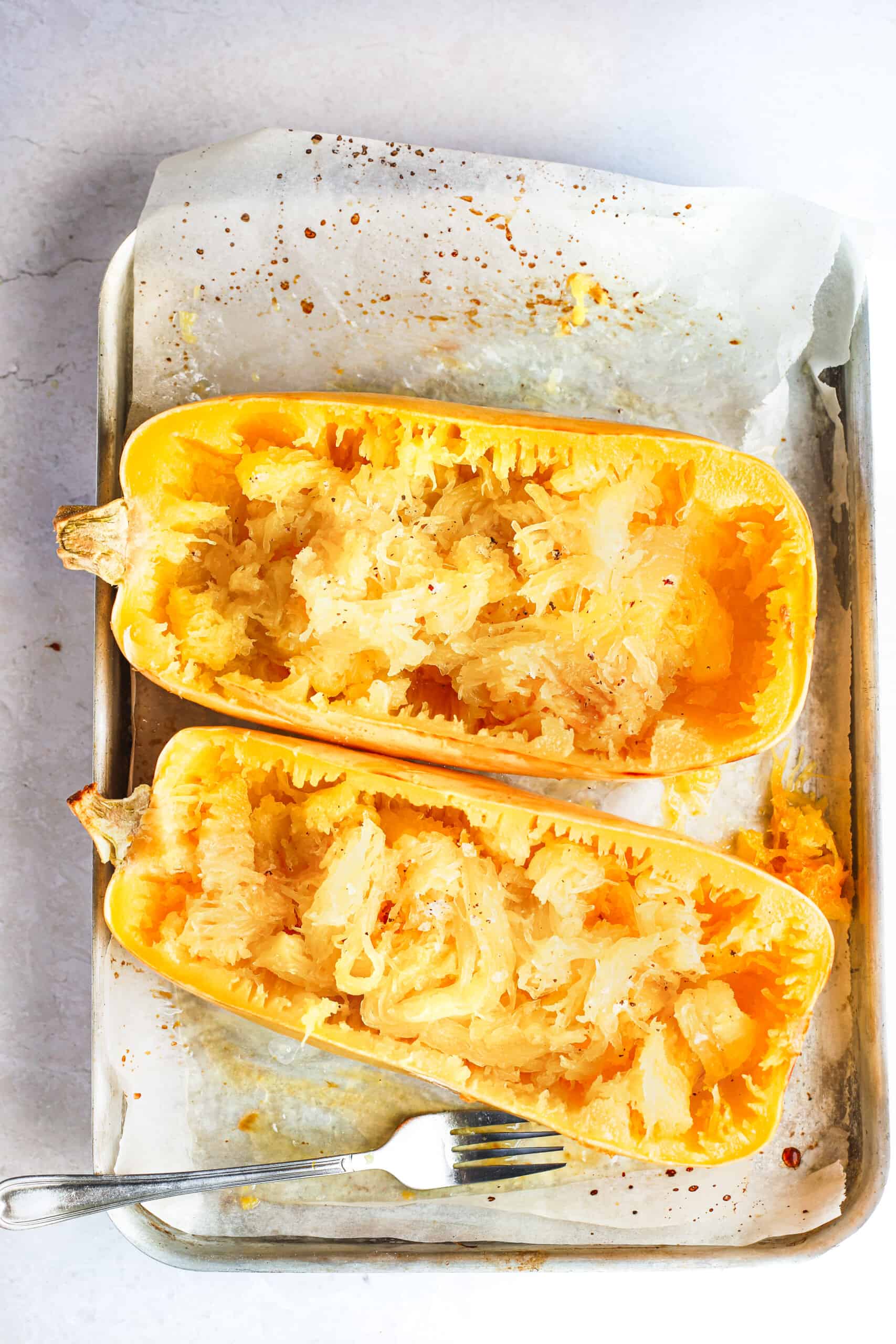 Two halves of a baked spaghetti squash on a parchment-lined pan with a fork