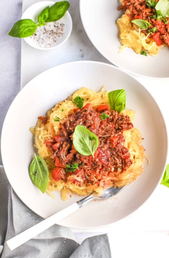 Gluten-free pasta topped with homemade bolognese sauce beside a dish of salt and pepper