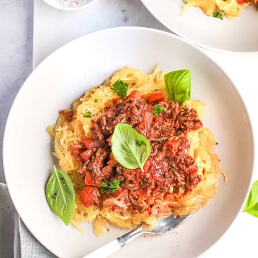 Gluten-free pasta topped with homemade bolognese sauce beside a dish of salt and pepper