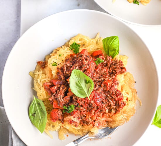 Gluten-free pasta topped with homemade bolognese sauce beside a dish of salt and pepper