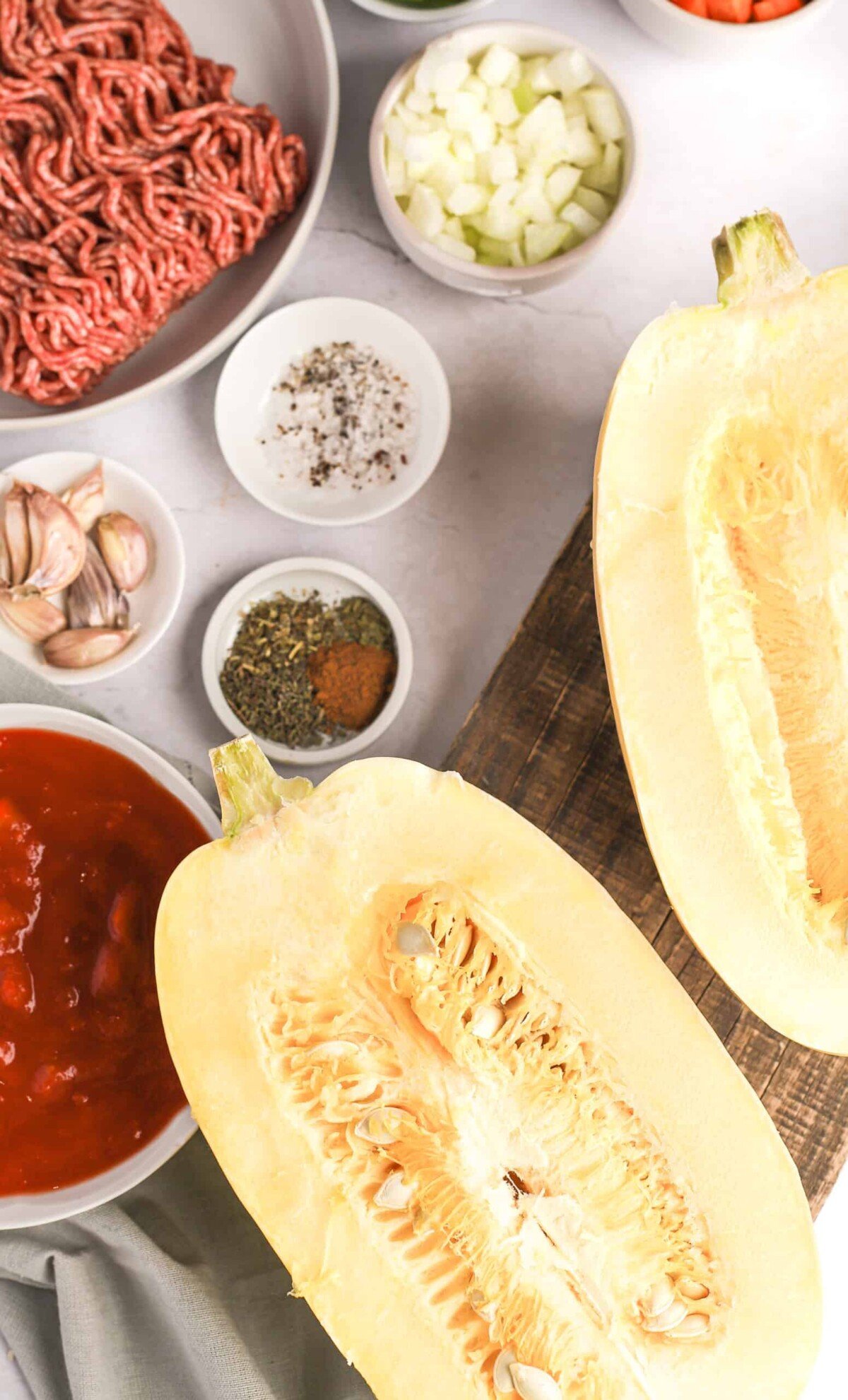 Ground beef, canned tomatoes, garlic cloves, spaghetti squash and the rest of the pasta ingredients on a table