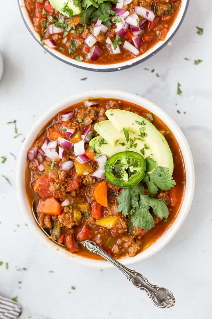 bowl of beef chili topped with avocado onions and cilantro