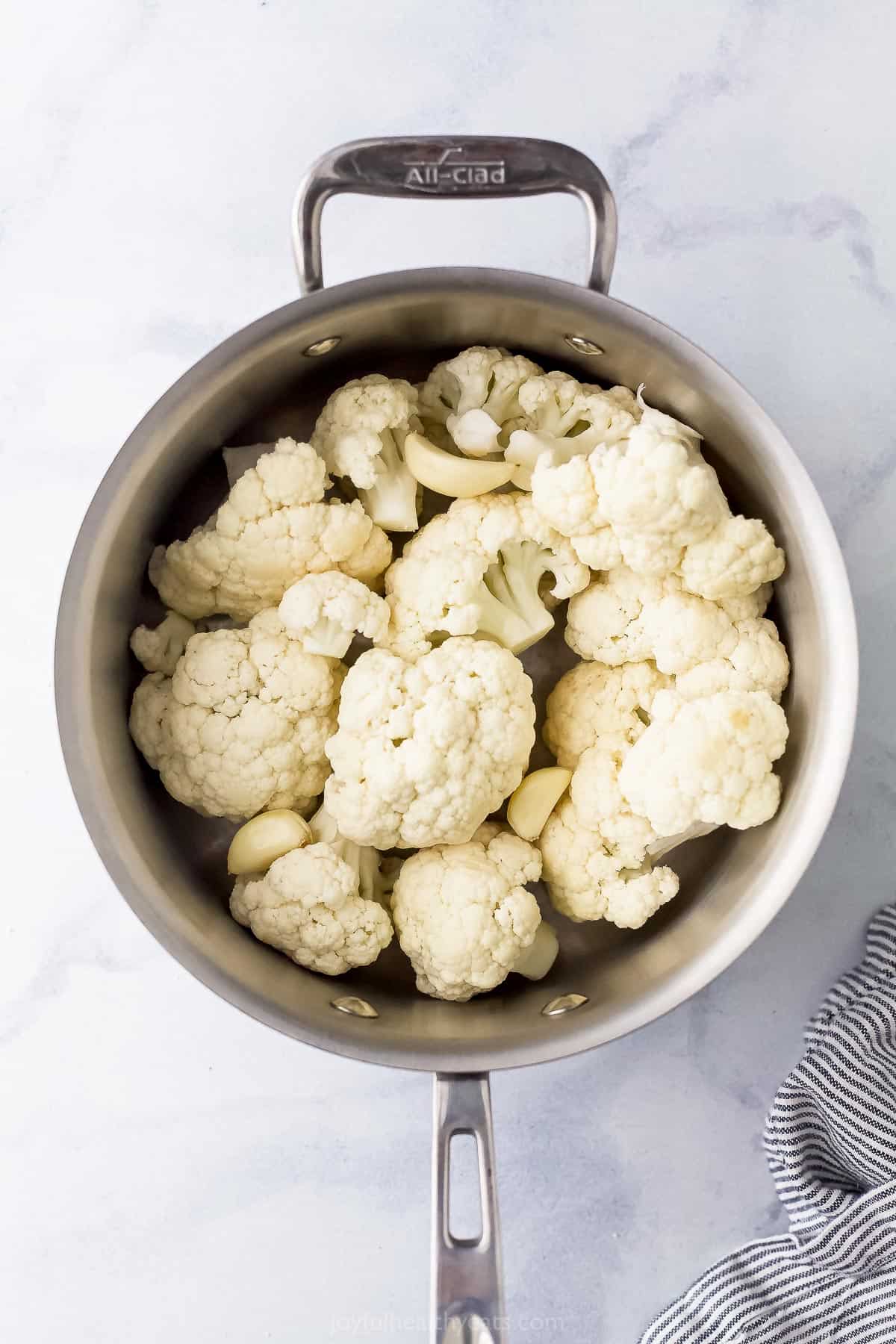 Uncooked cauliflower florets inside of a metal pot on a white surface