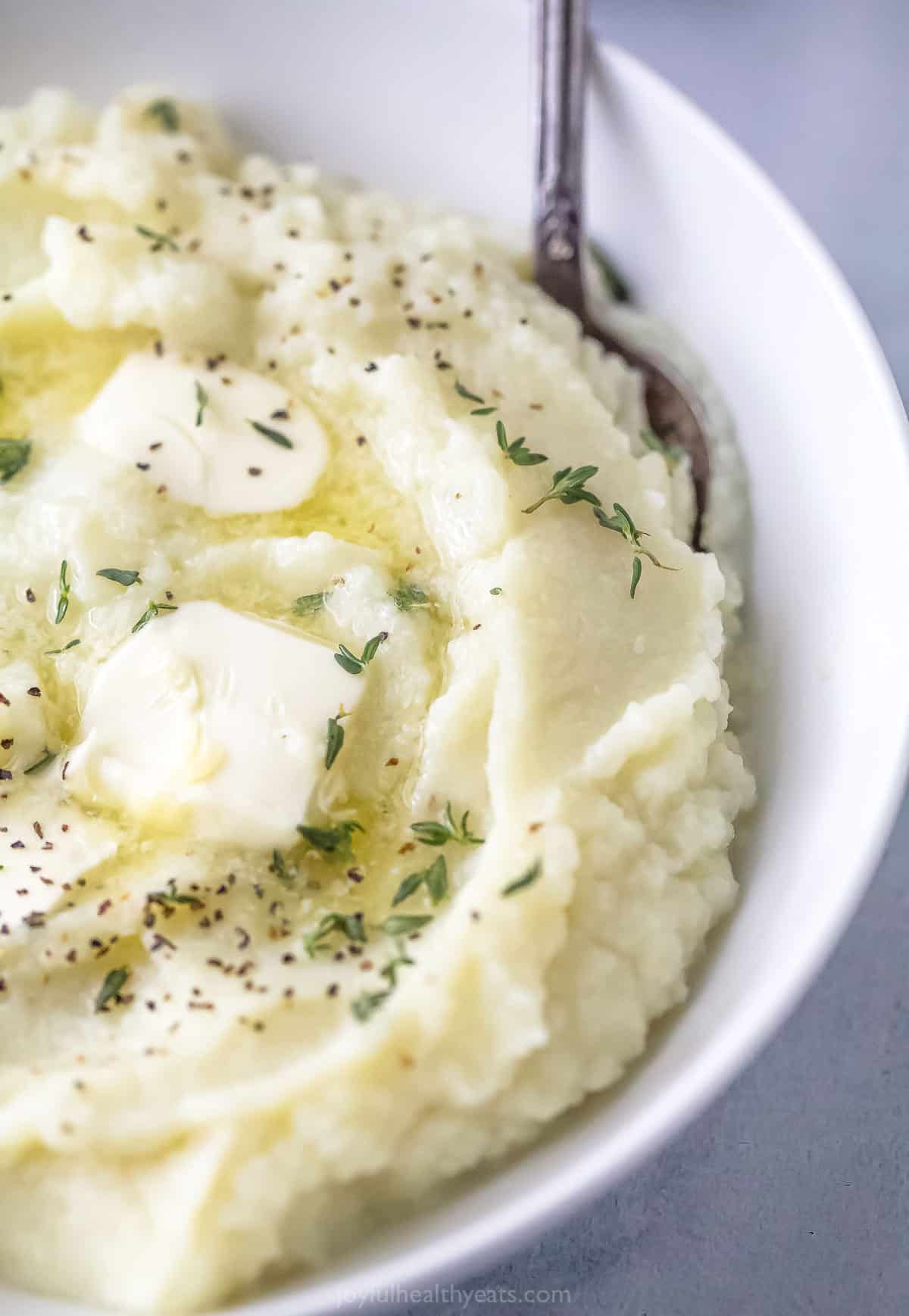 A metal spoon digging into a bowl of creamy mashed cauliflower