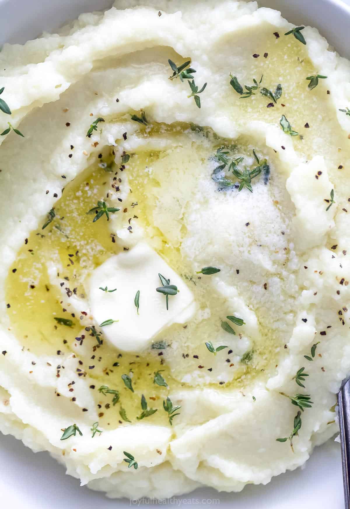 A bird's-eye view of cauliflower mash in a bowl with a pat of butter on top
