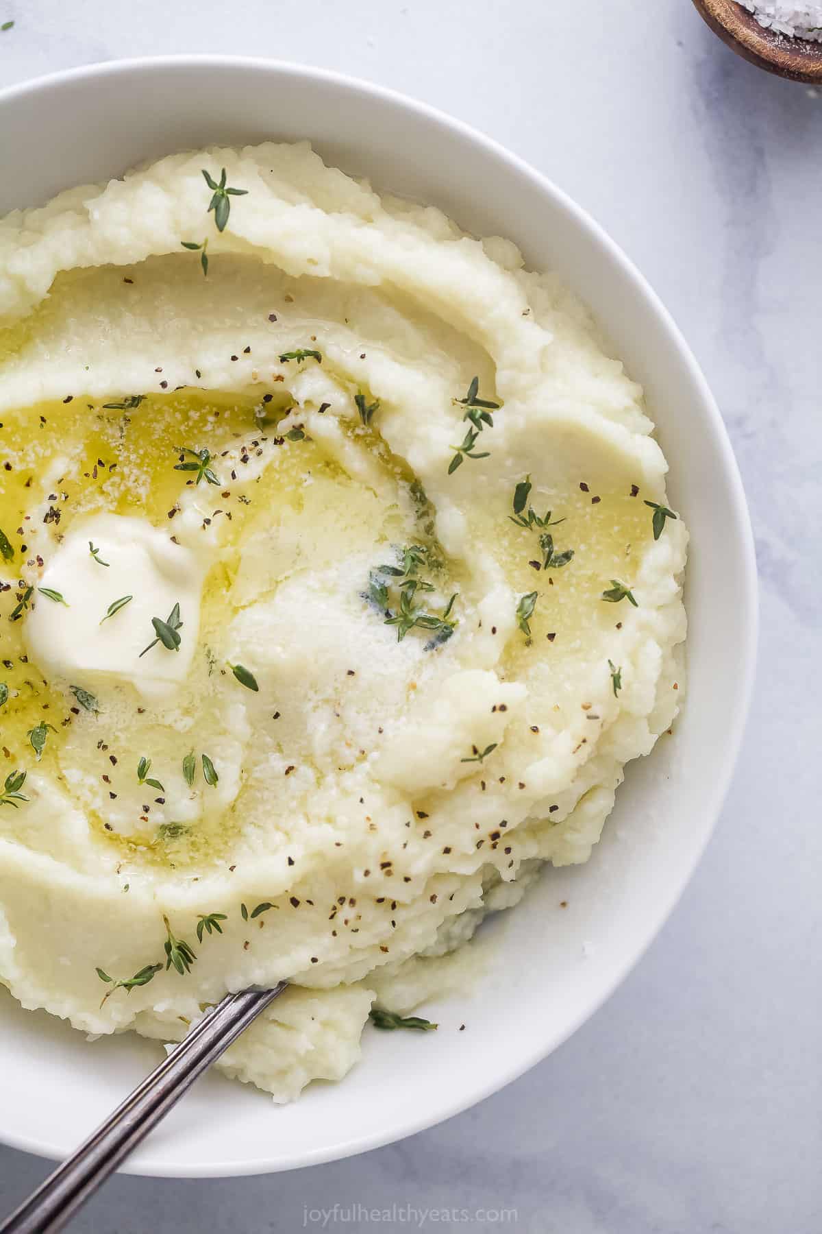 Mashed cauliflower in a large bowl with a metal serving spoon inside