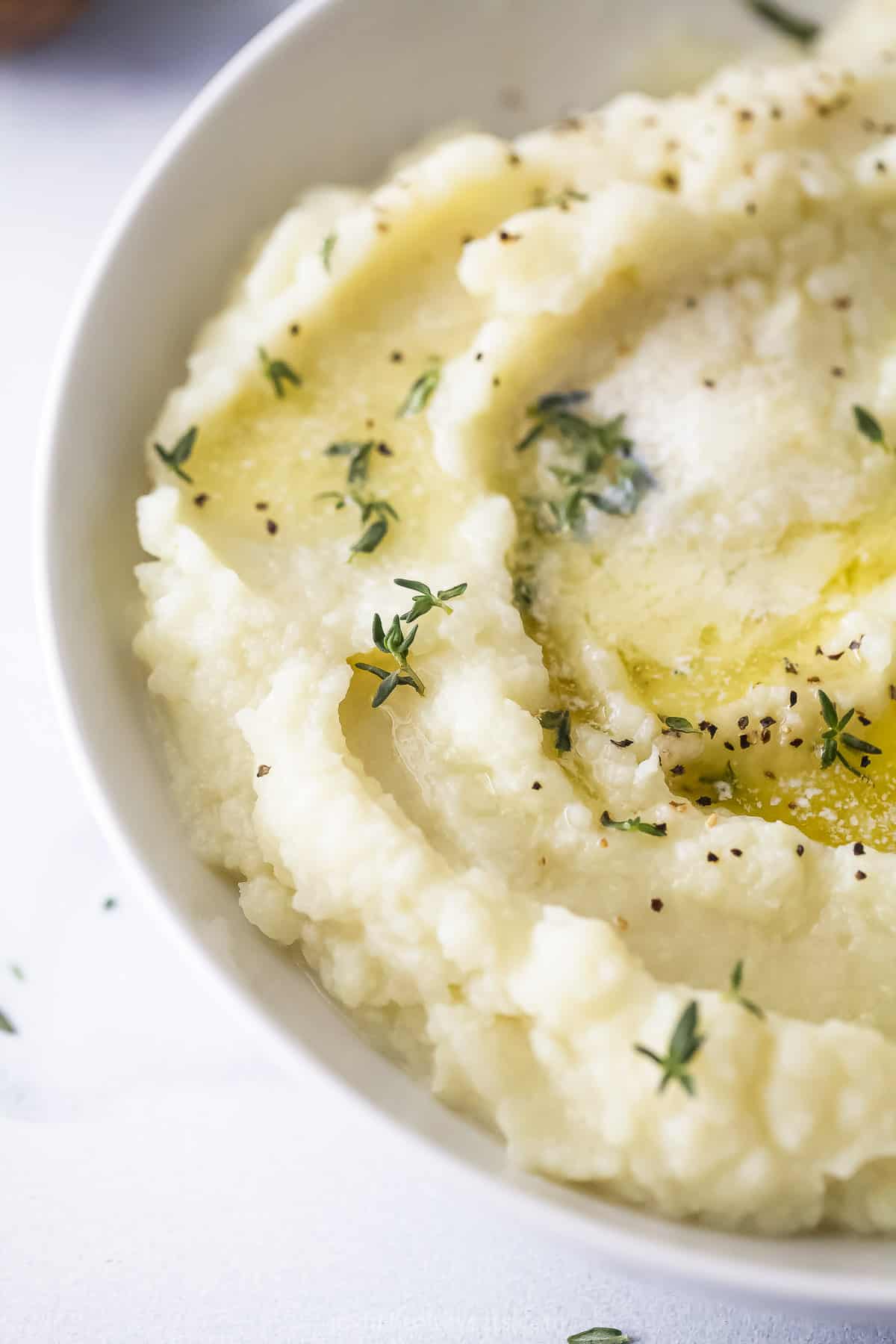 A close-up shot of a bowl of mashed cauliflower topped with butter and rosemary