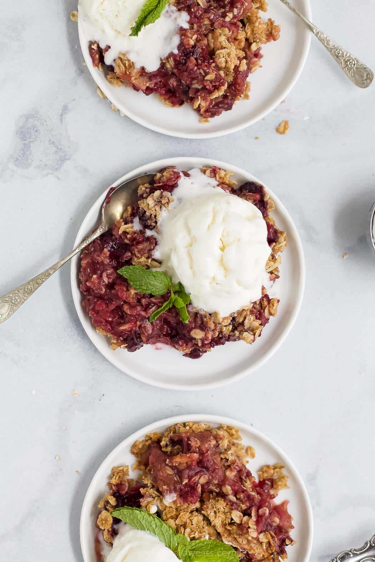 plates with apple blueberry crumble with ice cream and spoons