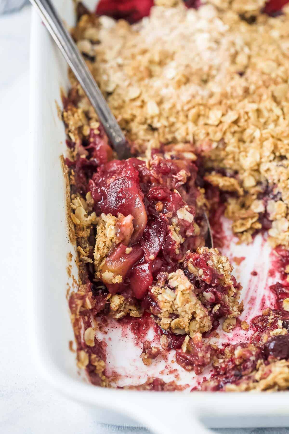 spoon scooping apple blueberry crumble from a baking dish