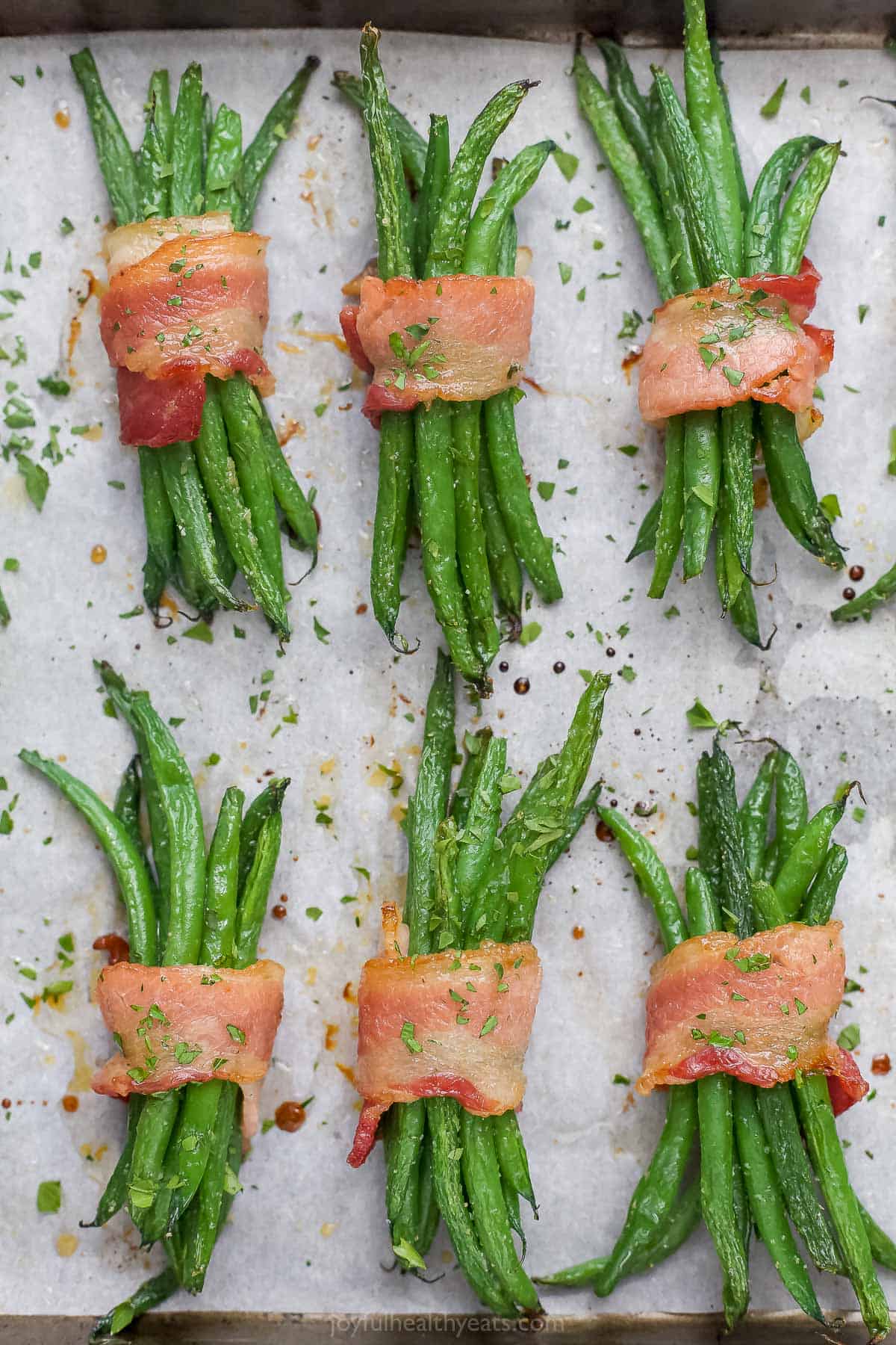 Six bacon green bean bundles lined up on a baking sheet lined with parchment paper