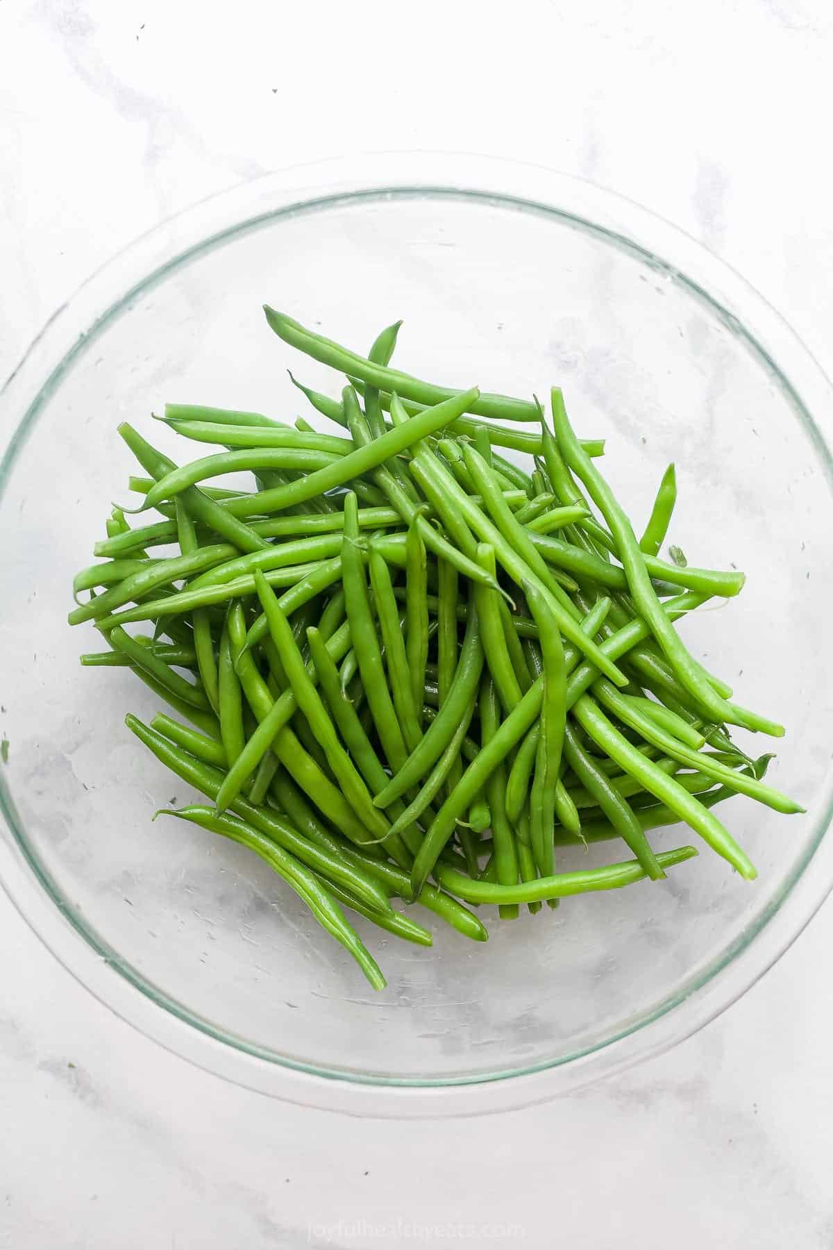 A glass bowl full of raw French green beans on a kitchen countertop