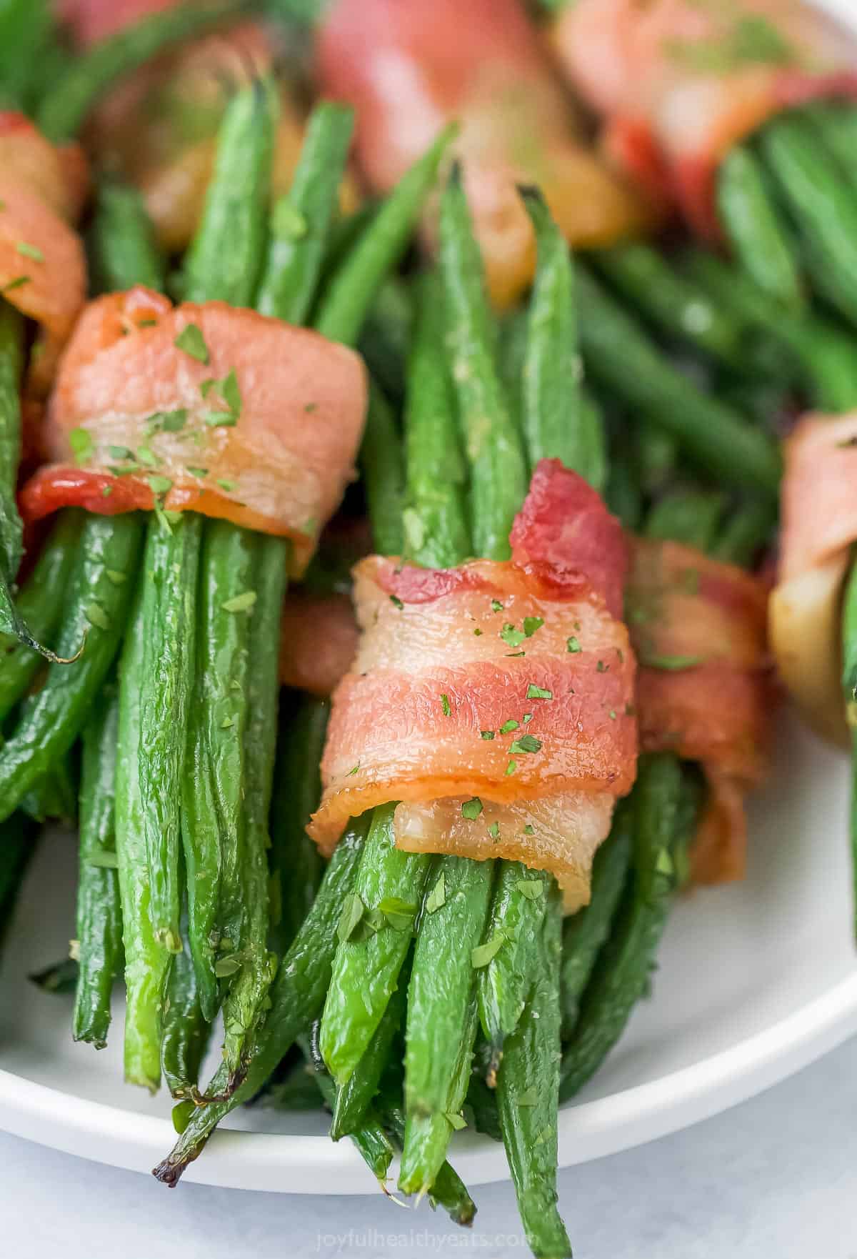 A close-up shot of a bundle of baked green beans wrapped inside a crispy strip of bacon