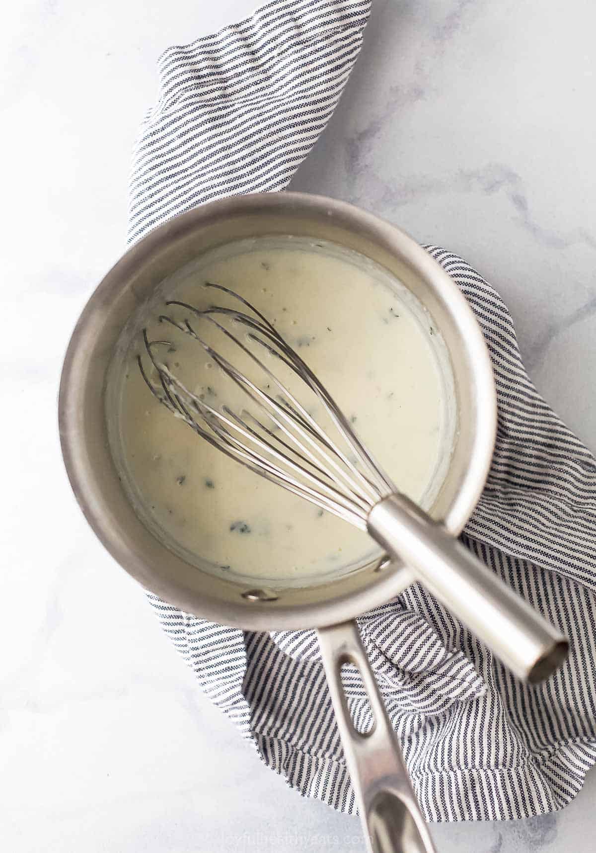 Cream sauce in a saucepan with a whisk.