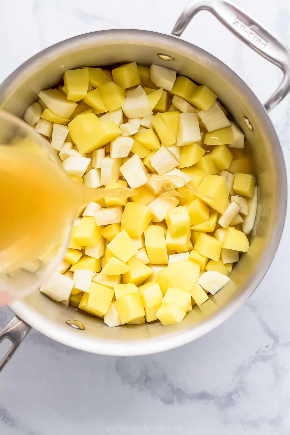 Chicken broth being poured into a pot containing diced parsnips and potatoes