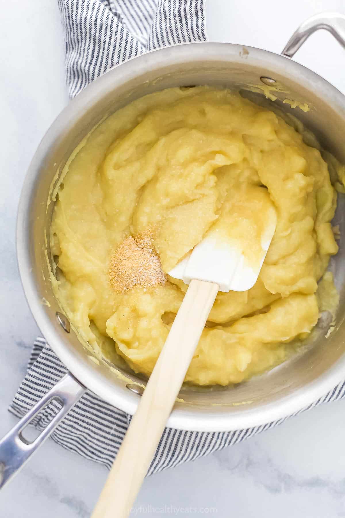 Parsnip mash in a pot being mixed with garlic powder using a rubber spatula