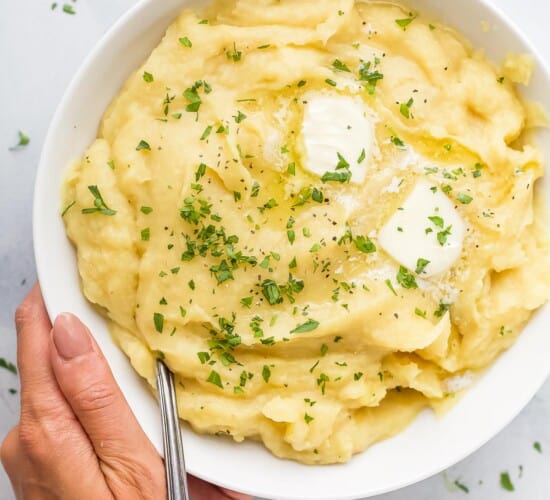A hand holding a large bowl of parsnip puree topped with butter and chopped parsley