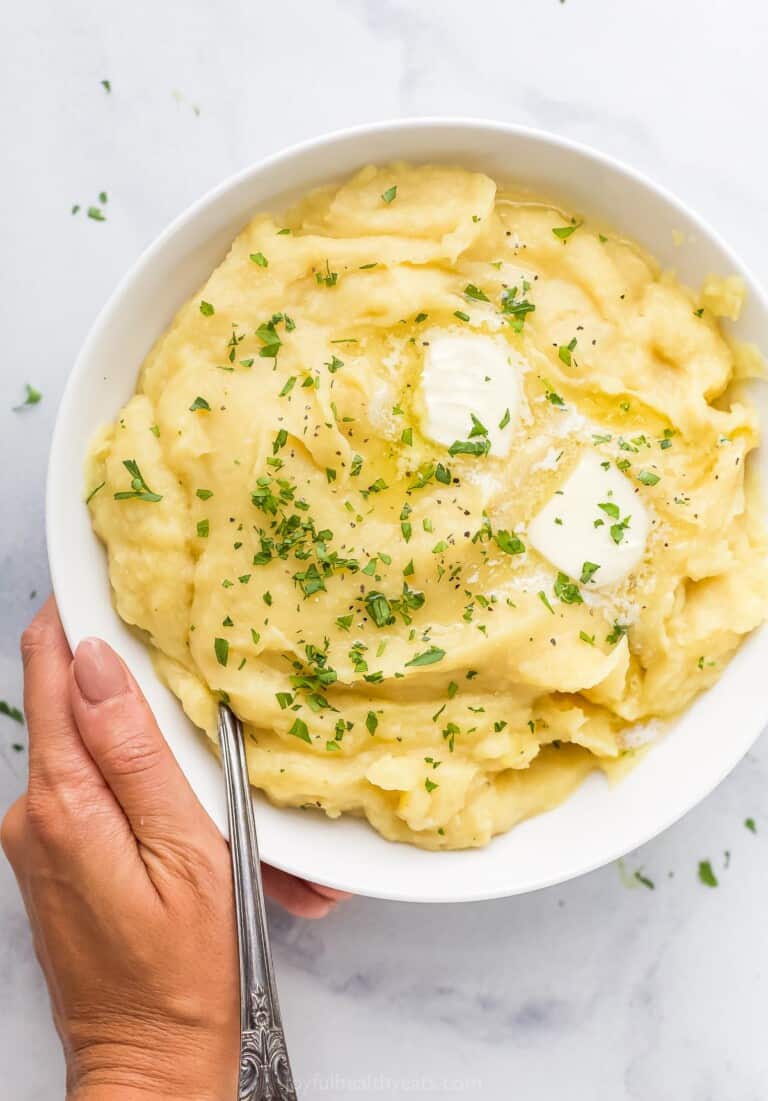 A hand holding a large bowl of parsnip puree topped with butter and chopped parsley