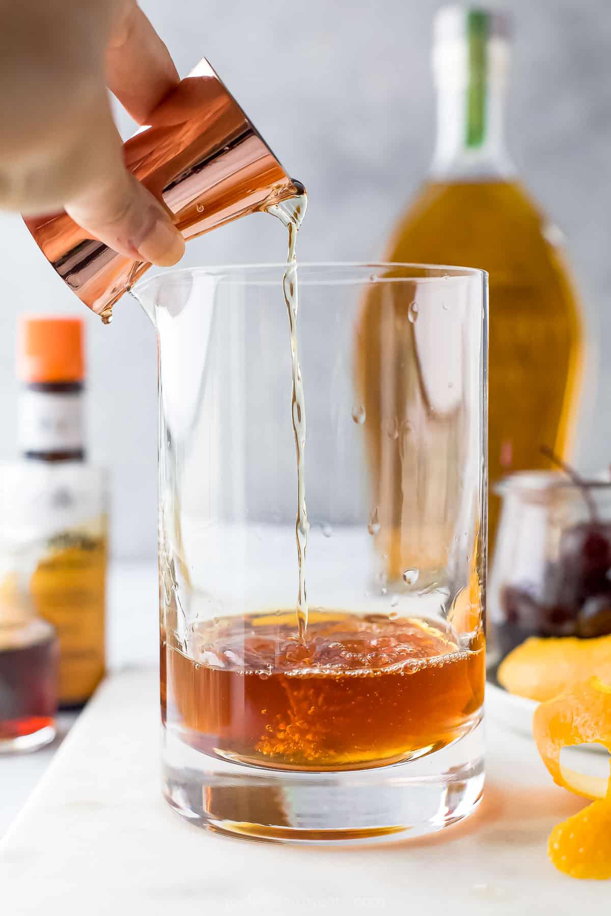 A couple ounces of bourbon being poured into a large glass cocktail shaker