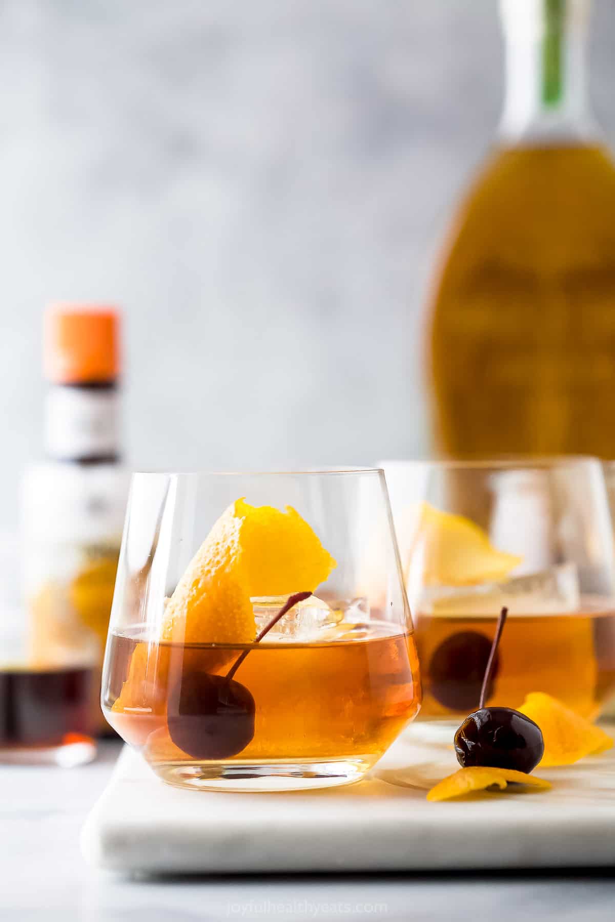 Two tumbler glasses on a cutting board with each one containing an old fashioned