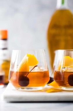 Two glasses of maple old fashioned cocktails on top of a white cutting board