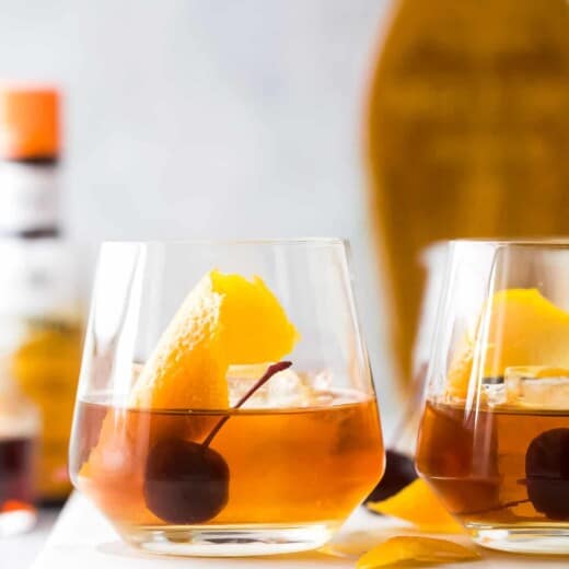 Two glasses of maple old fashioned cocktails on top of a white cutting board