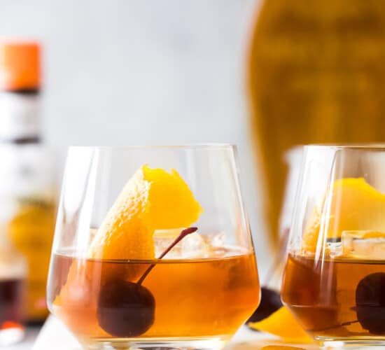 Two glasses of maple old fashioned cocktails on top of a white cutting board