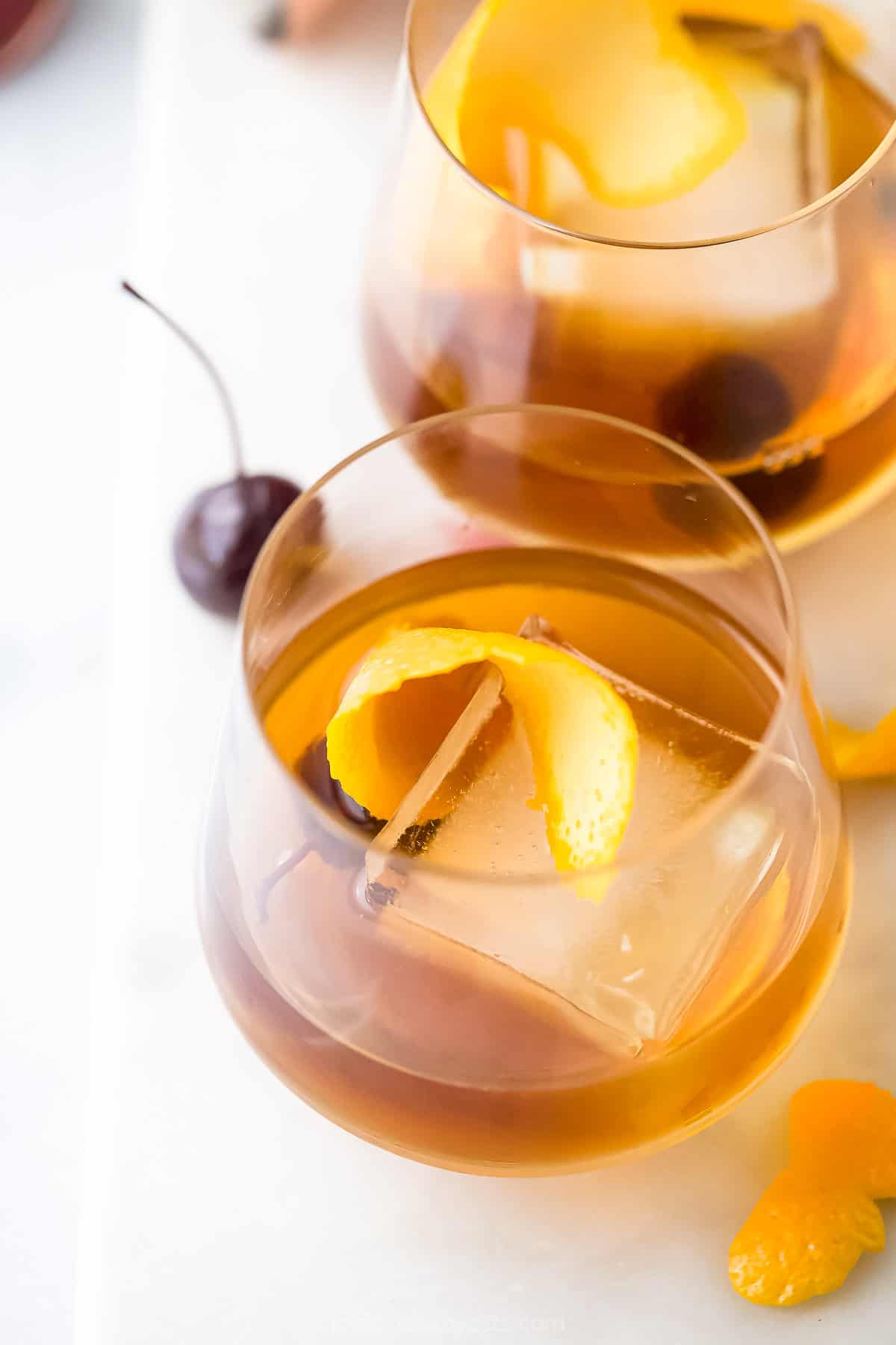 A close-up shot of a maple bourbon mixed drink in a glass with a cherry and an orange peel