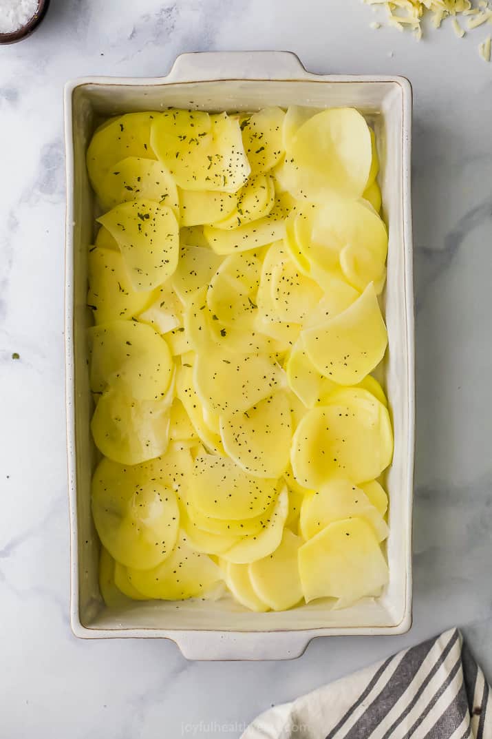sliced potatoes in a baking dish seasoned with salt and pepper