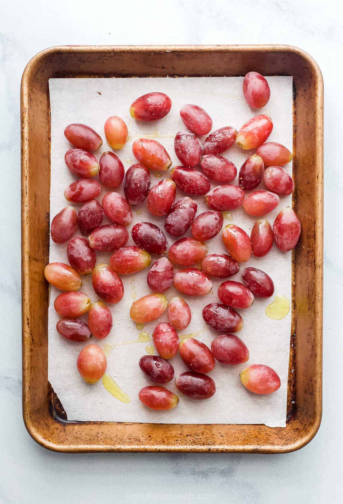 Red grapes covered in olive oil and seasoned with salt on a parchment-lined baking sheet
