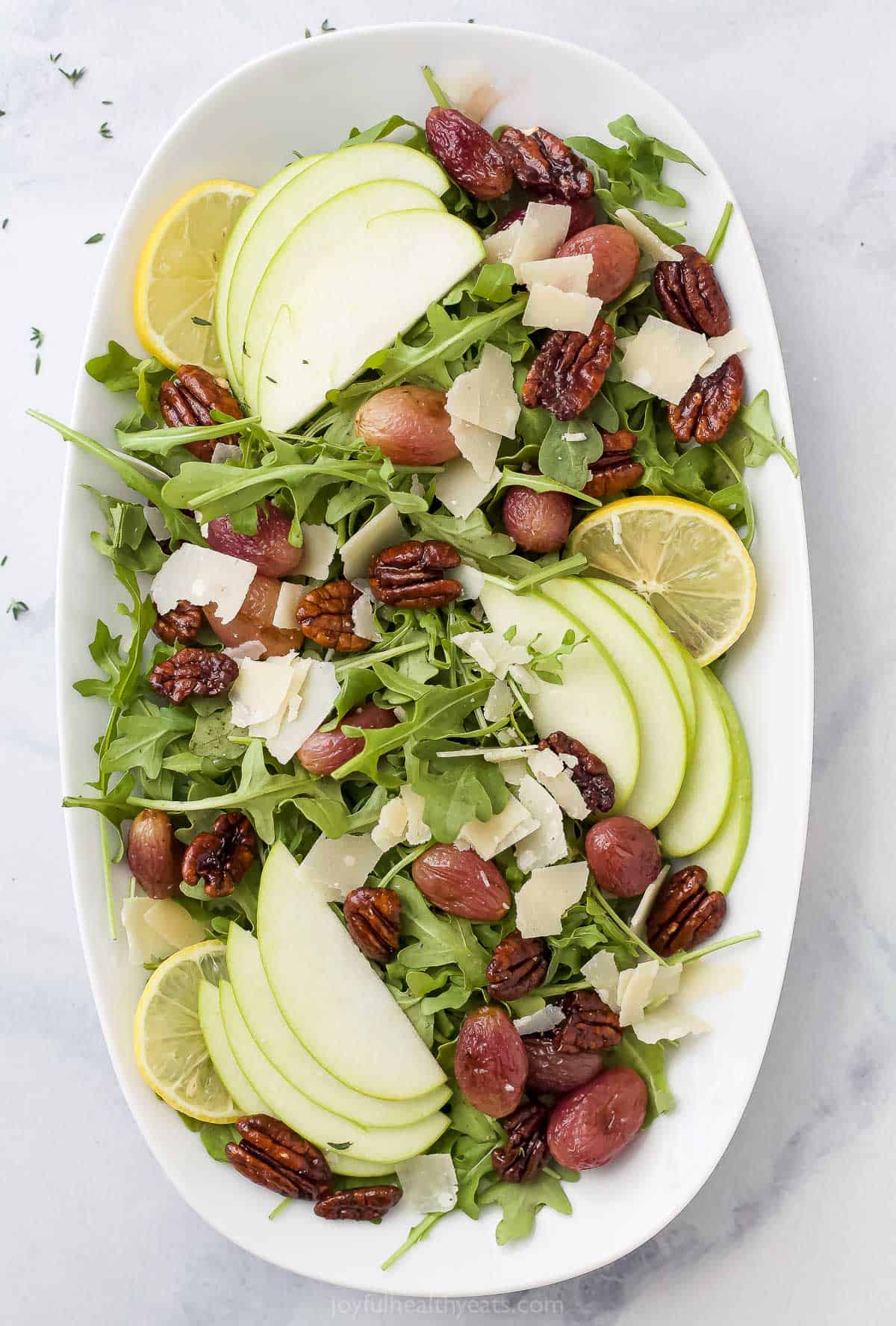 A large serving platter containing a fall salad with candied pecans, apple slices and roasted grapes