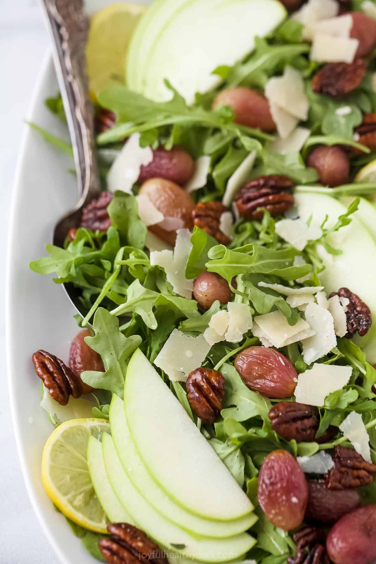 A close-up shot of an apple arugula salad in a serving dish with a spoon