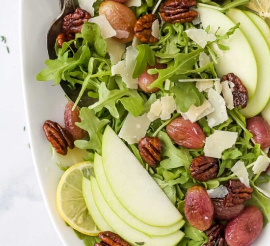 An arugula salad with roasted grapes and candied pecans inside of a large serving dish