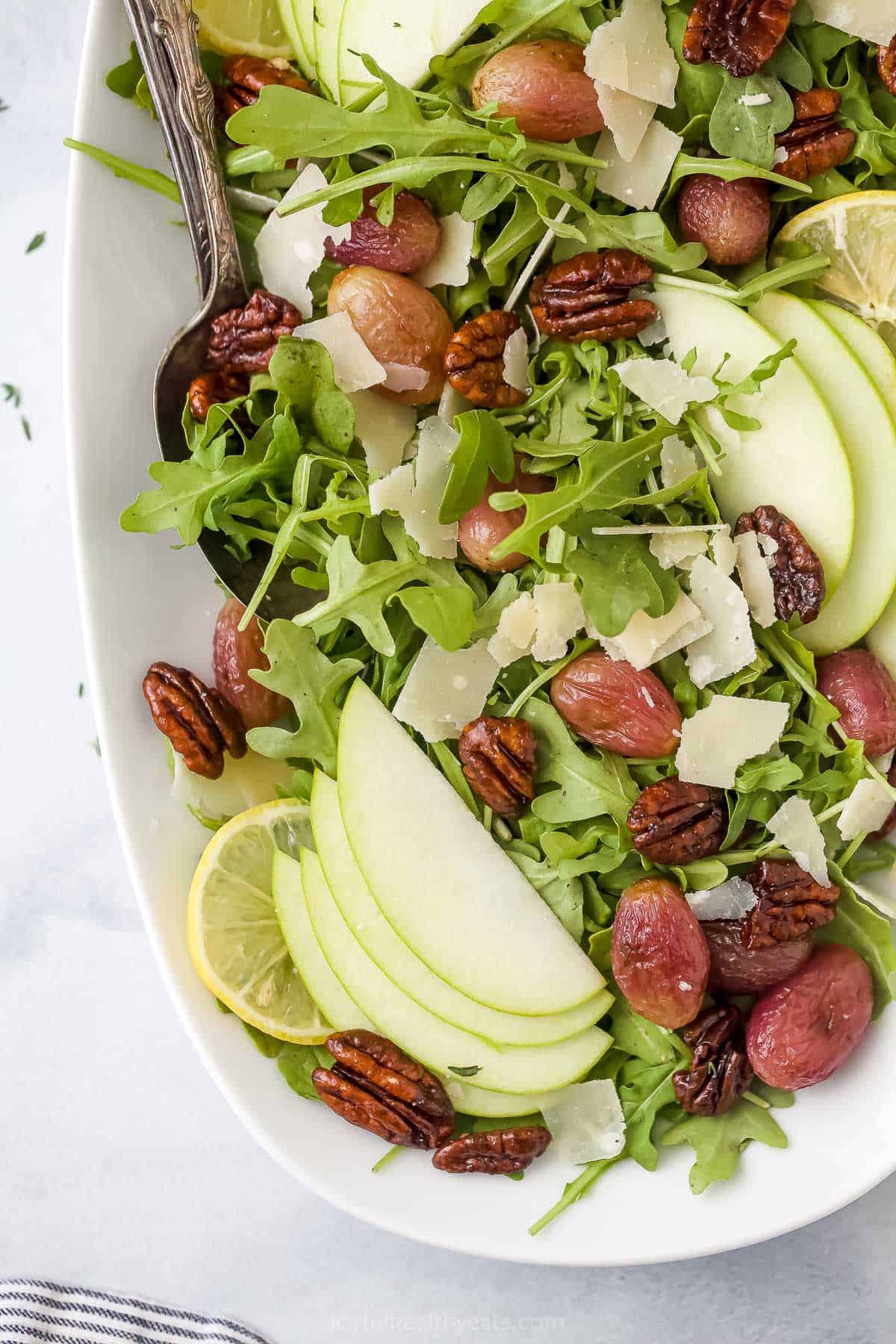 An arugula salad with roasted grapes and candied pecans inside of a large serving dish