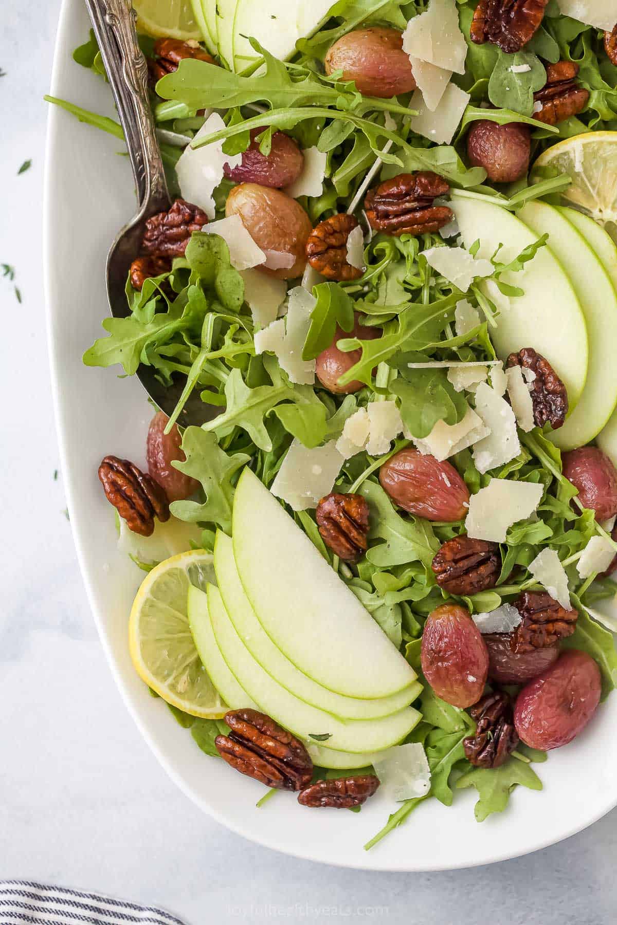 The bird's-eye view of a platter of arugula salad with roasted grapes, Parmigiano Reggiano cheese and candied pecans