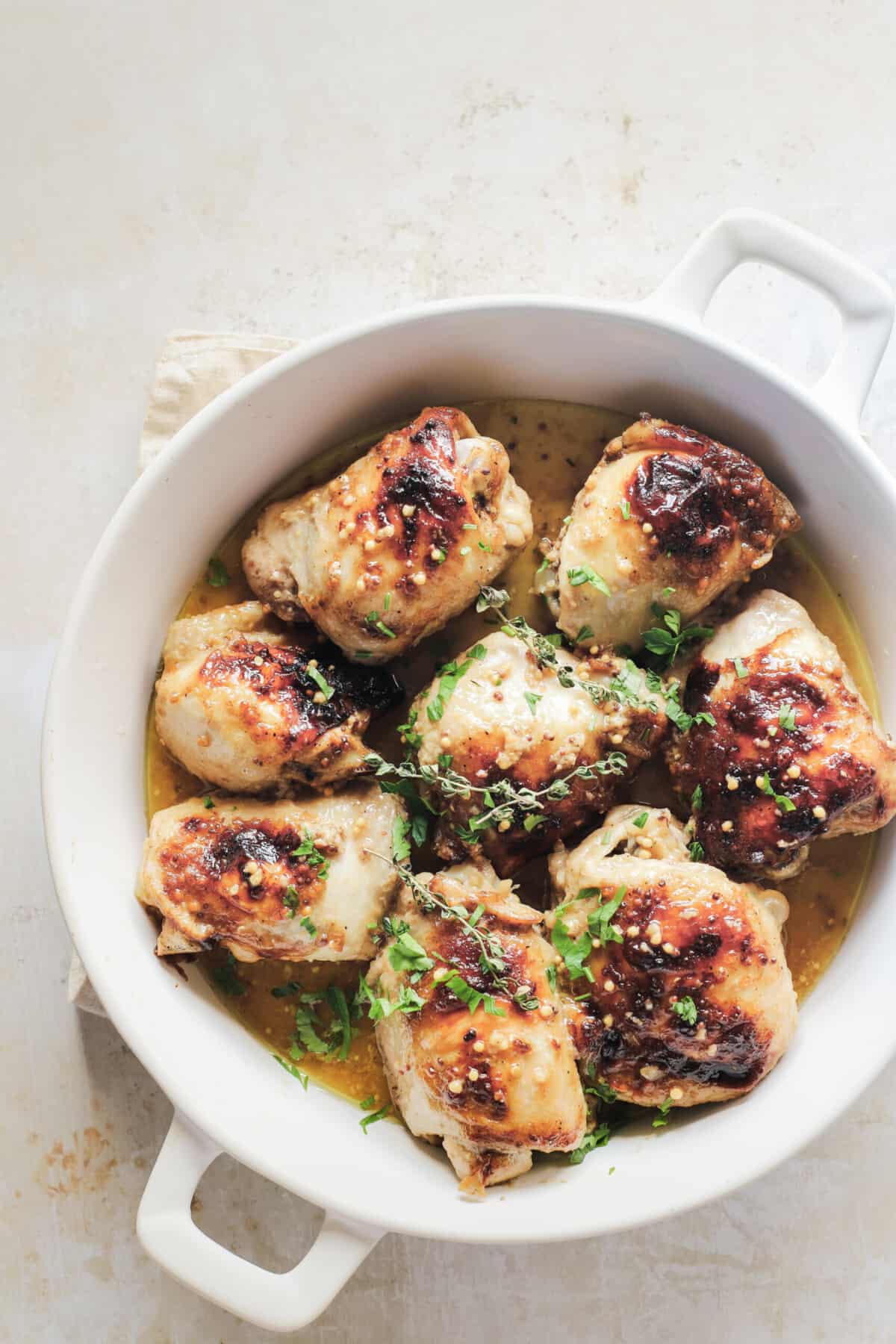 Eight roasted chicken thighs inside of a round baking dish on top of an off-white counter