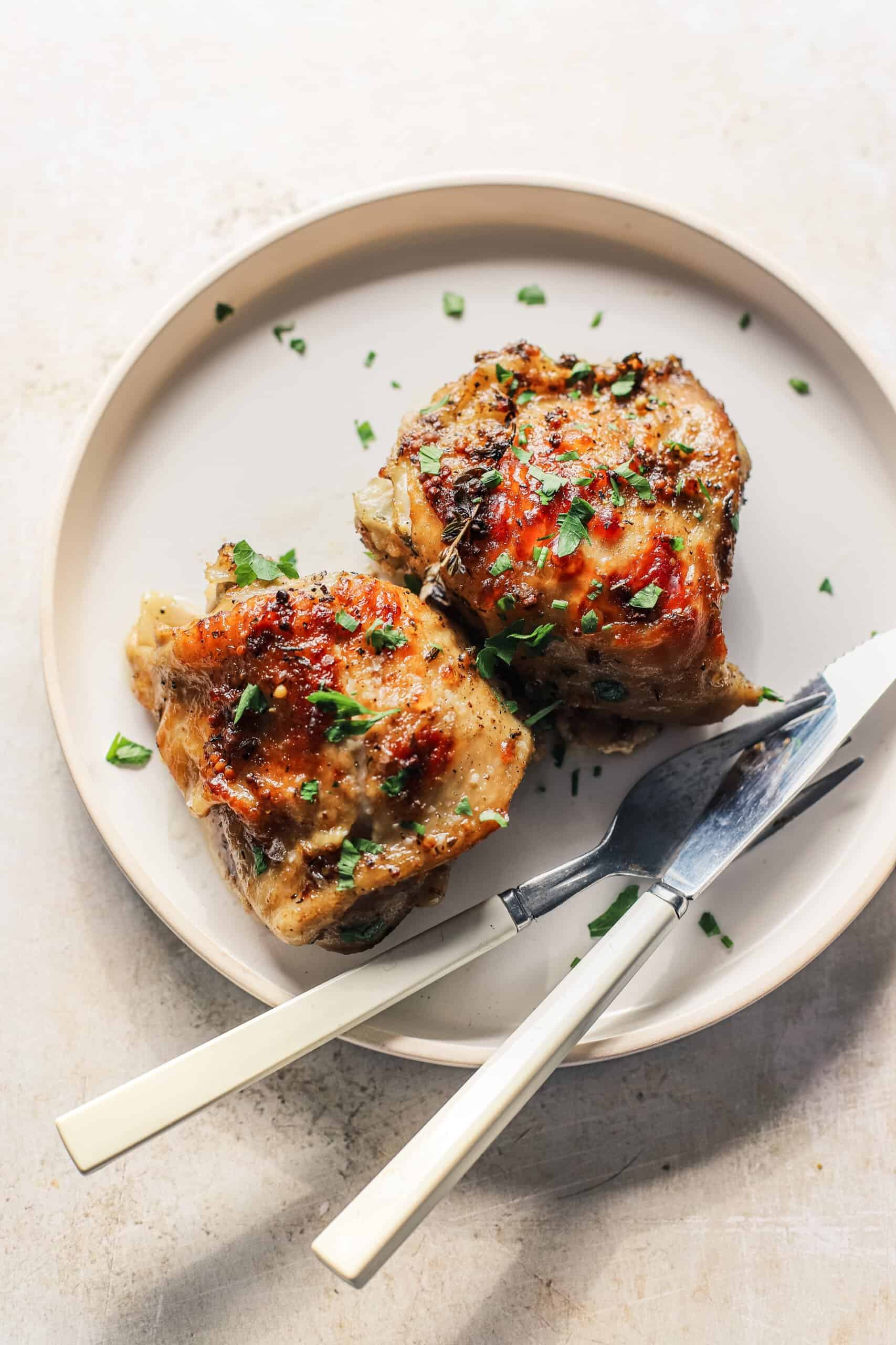 Two baked chicken thighs on a plate with a fork and knife