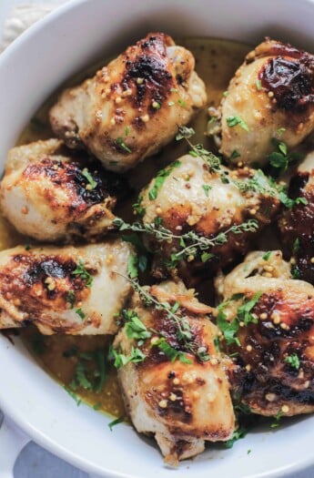 A close-up shot of freshly baked mustard glazed chicken thighs topped with fresh sage