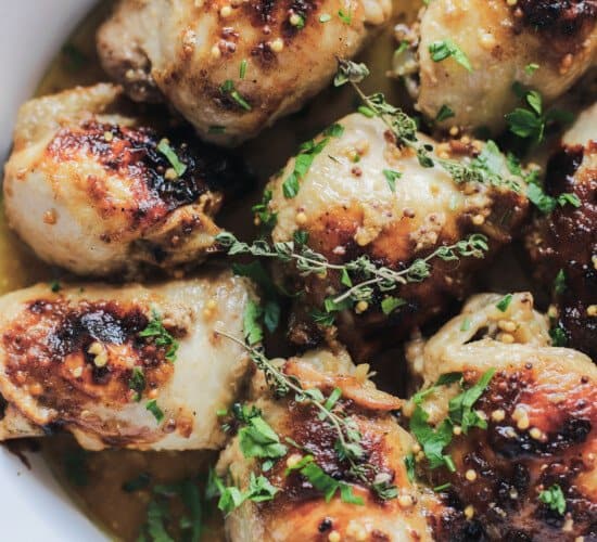 A close-up shot of freshly baked mustard glazed chicken thighs topped with fresh sage