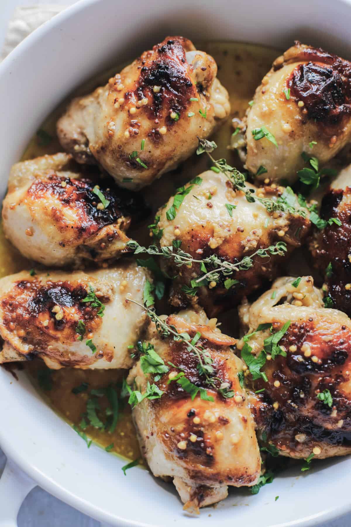 A close-up shot of freshly baked mustard glazed chicken thighs topped with fresh sage