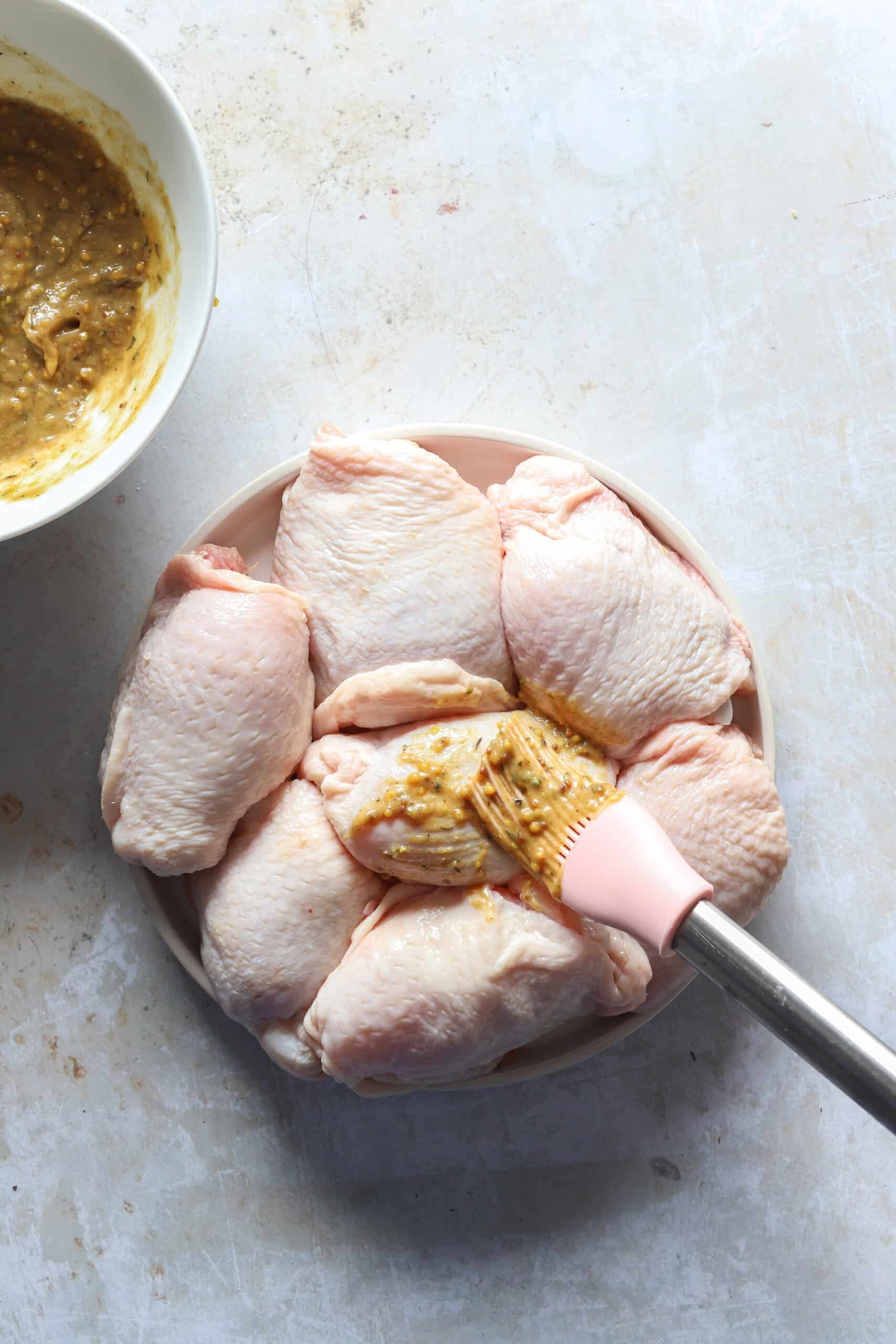 Raw chicken thighs on a plate being brushed with the seasoning mixture