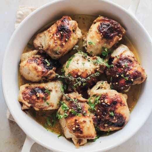 Eight mustard glazed chicken thighs inside of a white, round baking dish with handles