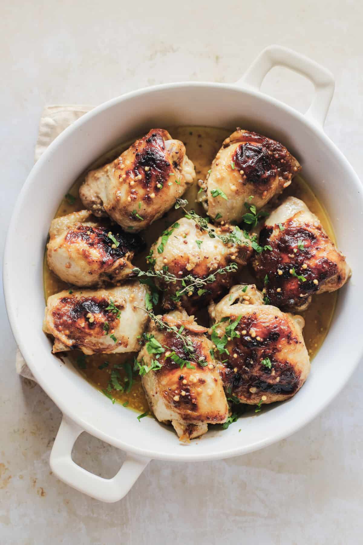 Eight mustard glazed chicken thighs inside of a white, round baking dish with handles