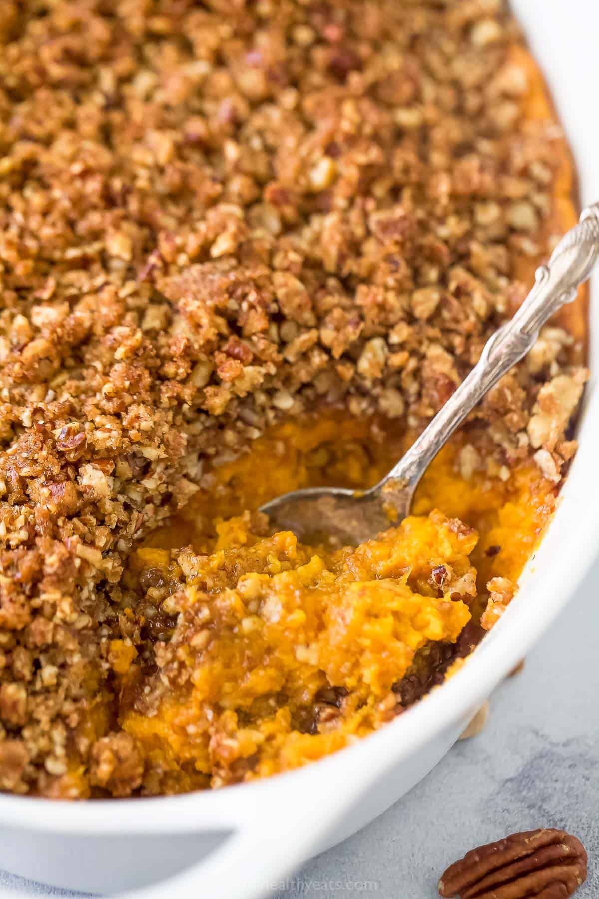 A close-up shot of a serving spoon scooping out a helping of sweet potato casserole from a baking dish